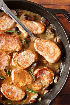 a skillet filled with meat and olives on top of a wooden table next to a fork