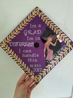 a hand holding up a purple and gold graduation cap that says i'm a grad