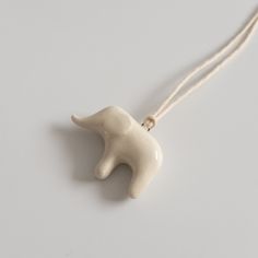 a white ceramic elephant ornament hanging from a string on a gray surface with a brown cord