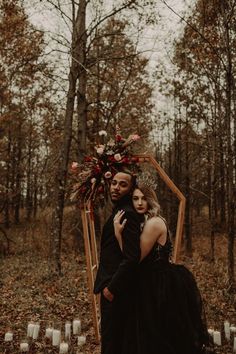 a man and woman standing next to each other in the woods with candles around them