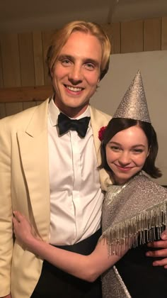 a man in a tuxedo is hugging a woman wearing a party hat and fringe shawl