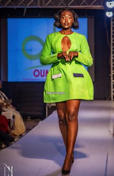 a woman is walking down the runway in a bright green coat and matching skirt with black heels