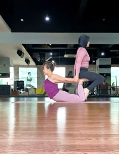 two women are doing yoga on the floor in a dance studio, one is holding her leg up