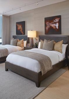 two beds in a hotel room with paintings on the wall and lamps on either side