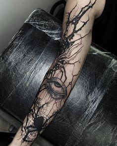 a man's arm with an eye and tree branches tattoo on the left forearm