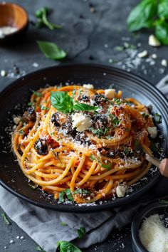 a plate of spaghetti with olives, parmesan cheese and basil on top