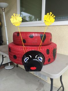 a table topped with three red tires covered in ladybug faces and yellow flowers