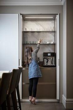 a woman standing in front of a refrigerator reaching up to get something on the counter