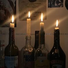 three bottles with candles in them sitting on a table next to some wine glasses and posters