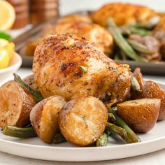 a white plate topped with chicken and potatoes next to lemon wedges on a table