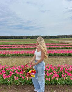 a woman standing in front of a field full of flowers holding a basket with eggs