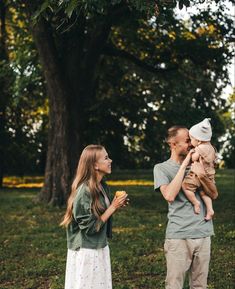 a man and woman holding a baby while standing in front of a tree