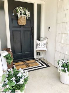 a black front door with white flowers and a welcome sign on the side walk next to it