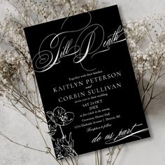 a black and white wedding card with flowers in the center on a marble table top