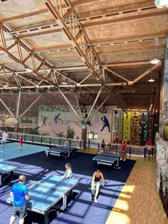 people playing ping pong in an indoor tennis court with wood beams and blue carpet