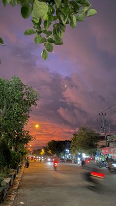 cars driving down the road at night time with clouds in the sky and trees lining the street