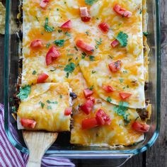 an enchilada casserole in a glass dish with a wooden spoon