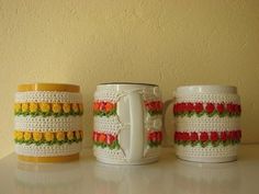 three crocheted coffee mugs are lined up on a table next to each other