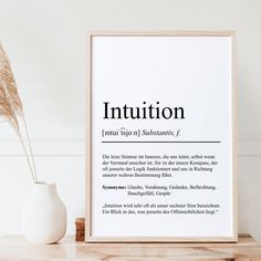 a white vase sitting on top of a wooden table next to a framed sign that says institution