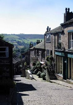 a cobblestone street in an old town with stone buildings and green fields behind it