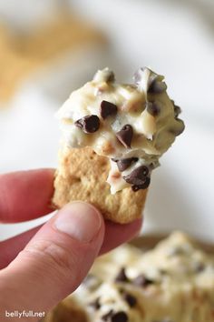 a hand holding a cookie with chocolate chips on it and white frosting in the middle