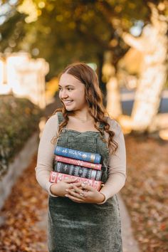 a woman standing in the leaves holding a stack of books