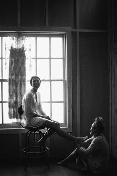 black and white photograph of two people sitting on stools in front of a window