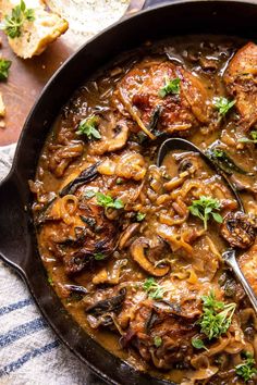 a skillet filled with meat and mushrooms covered in gravy, garnished with parsley