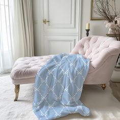 a white and blue blanket sitting on top of a pink chair next to a window