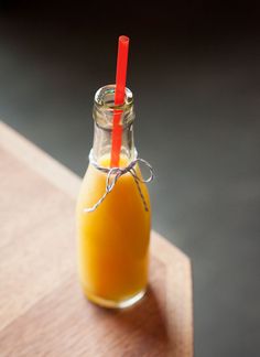 a glass bottle filled with liquid sitting on top of a wooden table next to a red straw