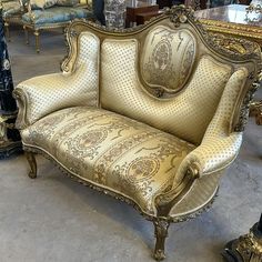 an ornate gold couch sitting on top of a floor next to other antique chairs and tables