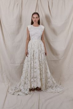 a woman standing in front of a white backdrop wearing a dress with flowers on it