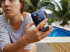 a woman holding a cell phone next to a swimming pool with palm trees in the background