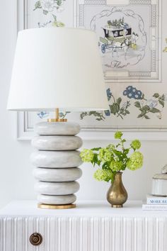 a lamp on top of a white table next to a vase with flowers in it