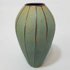 a green vase sitting on top of a white table next to a black container with brown lines