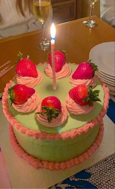 a green cake with strawberries on it and a lit candle