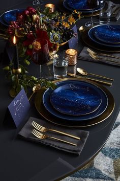 the table is set with blue plates and gold place settings for two people to sit at