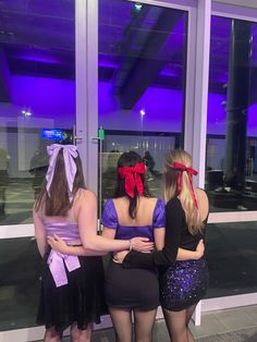 three women standing in front of a window with their backs to the camera and wearing bows