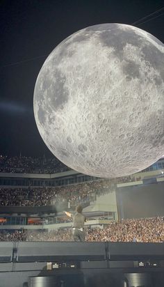 a man standing on top of a stage in front of a giant moon above a crowd