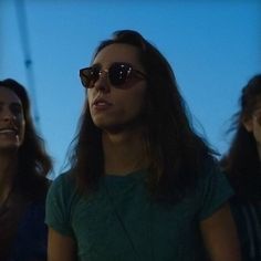 three women wearing sunglasses are standing in front of the camera and one is looking off into the distance