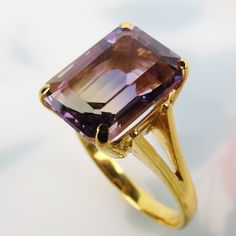 "A delightful golden purple 4 carat ametrine gemstone tops this vintage 1970s 14k yellow gold ring. Rarely found in nature, Ametrine is a quartz crystal with the presence of both amethyst and citrine. This bi-color quartz gem has 80/20 split zones of purple amethyst and yellow citrine. The citrine appears as a band with more purple surrounding it. The 11.2mm x 8.2mm x 6.2mm emerald-cut ametrine has nice translucency and clarity.  Four sturdy prongs hold the gem above a classic basket setting. Th Yellow Gold Emerald-cut Amethyst Ring For Formal Occasions, Formal Faceted Amethyst Ring Fine Jewelry, 14k Yellow Gold Emerald-cut Amethyst Ring, Faceted Amethyst Ring In Yellow Gold Fine Jewelry, Elegant Faceted Amethyst Ring In Yellow Gold, Classic Yellow Gold Amethyst Ring With Diamond Cut, Elegant Gold Solitaire Amethyst Ring, Formal Gold Amethyst Ring With Diamond Cut, Faceted Purple Amethyst Ring For Formal Occasions