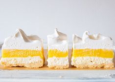 three pieces of cake sitting on top of a wooden cutting board with icing and whipped cream