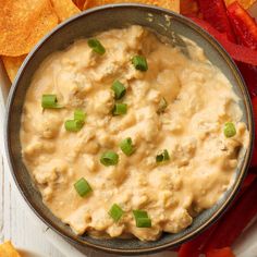 a bowl filled with dip surrounded by tortilla chips and bell pepper wedges