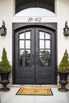 the front door to an apartment building with two potted plants in front of it