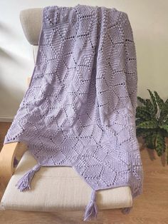 a purple crocheted blanket sitting on top of a white chair next to a potted plant