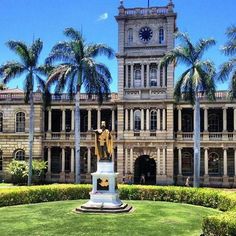 a large building with a clock on the front and palm trees in the back ground