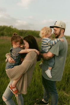 a man, woman and two children are standing in the grass with their arms around each other