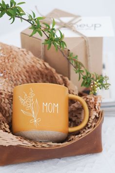 a yellow coffee mug sitting on top of a wooden tray next to a box and plant