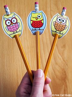 three pencils in the shape of cartoon characters are held by a person's hand