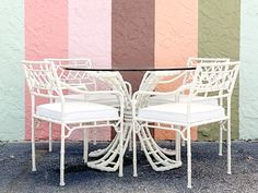 two white wicker chairs and a glass table against a multi - colored striped wall